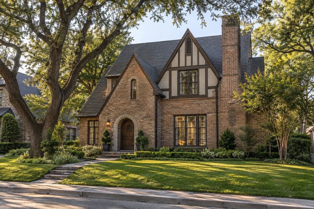 A brick Tudor-style home under mature live oaks, typical of older Dallas neighborhoods